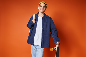 charismatic young man in casual outfit standing with skateboard against terracotta background