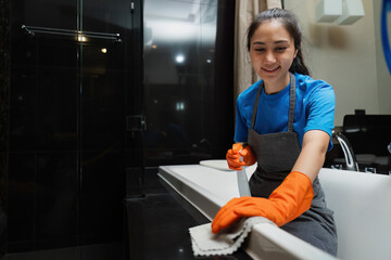 Cleaning online service. yong woman housekeeper cleaning bathtub in bathroom with a cloth. House...