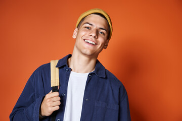 portrait of smiling handsome guy in yellow hat with backpack against terracotta background