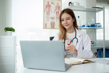 Young Asian doctor in white medical uniform with stethoscope using laptop computer video chatting...