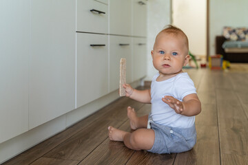 Cute one year old boy sitting in the kitchen with fresh bread. Child with bread on the floor....