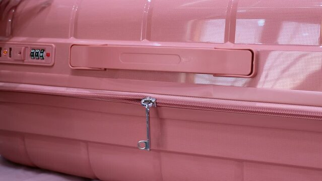 Female hands unpacking pink suitcase by unzipping travel luggage in hotel room. Open baggage zip close up