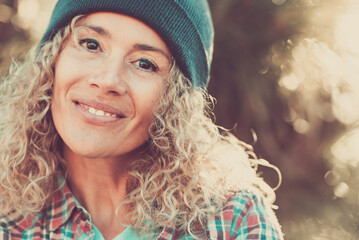 Middle age beautiful woman portrait with hipster style and warm woolen hat in outdoor with defocused bokeh nature background - cheerful happy people female caucasian looking at camera - obrazy, fototapety, plakaty