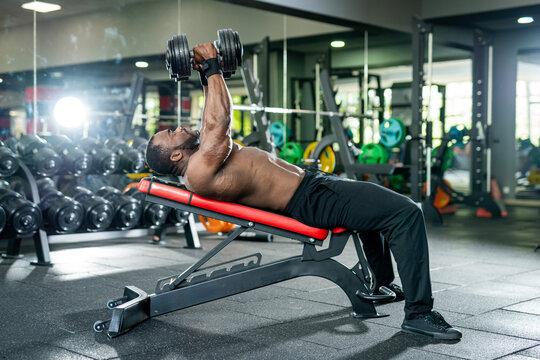 Muscular man is doing bench press with dumbbells in the gym.