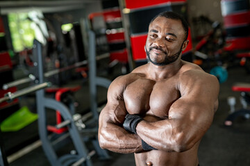 Fototapeta na wymiar Portrait of muscular african american man posing with dumbbells in gym