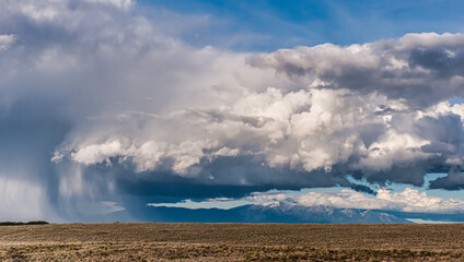 Striking image showcasing an impending storm with dramatic clouds over a sparse, desolate landscape and distant mountains
