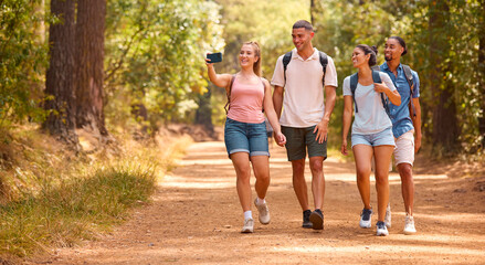 Young Active Couple With Friends Hiking Along Trail In Countryside Recording Video On Mobile Phone