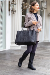 Beautiful woman in fashion outfit with black boots and big python handbag