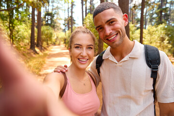 POV Shot Of Couple Hiking Along Trail Through Countryside Posing For Selfie On Mobile Phone