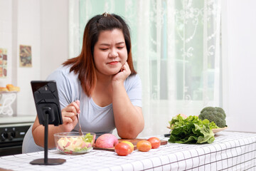 Obraz na płótnie Canvas Fat Asian woman cooking in the kitchen. Female blogger create cooking content Online on social media via smartphone. weight loss food