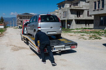 A man loading a broken down car onto a tow truck. Roadside assistance concept.