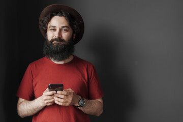 A casually dressed bearded man deeply focused on his smartphone. His style reflects a modern,...