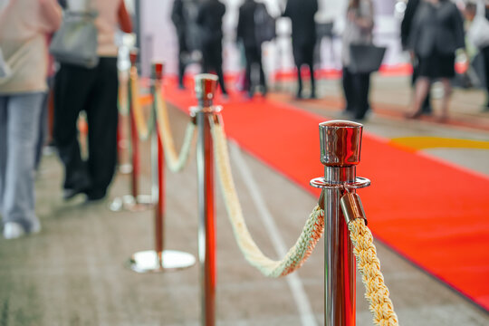 Rope fencing with gold pillars with a red carpet for celebrities and guests of an expensive event with crowds of people.