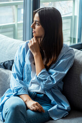Depressed young woman sitting on couch in the living room at home, Frustrated confused female feels...