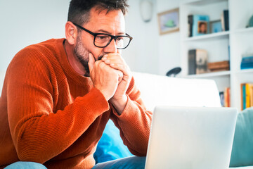 Focused adult Caucasian man in glasses sit on sofa at home work online on laptop gadget....