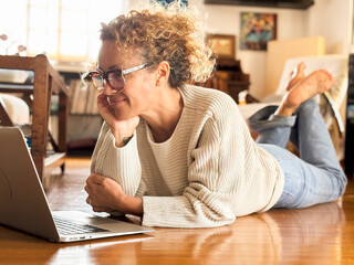 One woman lay down on the floor at home using laptop computer smiling at screen. People and searching on web. Alternative small business workplace indoor leisure activity alone. Wireless connection