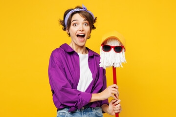 Young shocked excited woman wear purple shirt casual clothes do housework tidy up hold in hand mop...