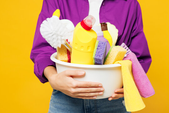 Close up cropped photo shot young woman she wearing purple shirt hold basin with detergent bottles do housework tidy up isolated on plain yellow background studio. Housekeeping cleaning home concept.