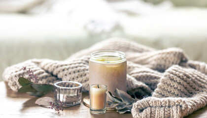 Cozy composition with candles and a knitted element on a blurred background.