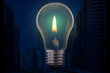 Light bulb with candle burning inside against a modern city district without electricity at night....