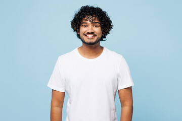 Young smiling satisfied positive cheerful happy Indian man he wear white t-shirt casual clothes looking camera isolated on plain pastel light blue cyan background studio portrait. Lifestyle concept.