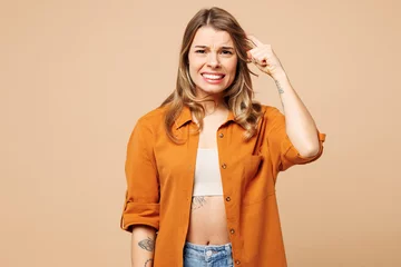 Young shocked mistaken sad Caucasian woman wear orange shirt casual clothes look camera hold scratch head look camera isolated on plain pastel light beige background studio portrait Lifestyle concept © ViDi Studio