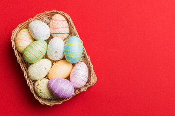 Colorful Easter eggs in wicker basket against colored background, closeup. top view with copy space