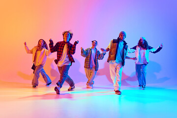 Positive young people, men and women in sport style clothes dancing contemporary dance styles over gradient studio background in neon. Concept of modern dance, hobby, active lifestyle, youth culture