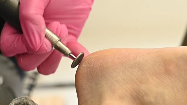 Woman on professional pedicure procedure by abrasive disc machine in beauty salon. 