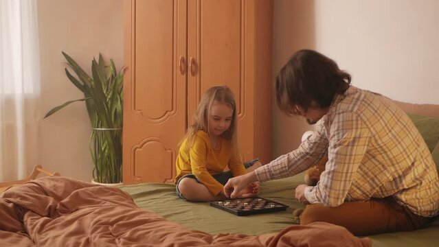 Joyful dad and little girl have fun with checkers