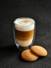 A glass of delicious latte and cookies on a black background. Delicious latte macchiato and cookies. Close-up