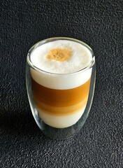 Glass mug with cappuccino isolated closeup on a black background. A cup of coffee. Hot coffee with...