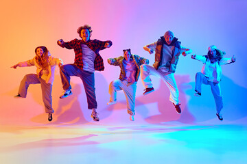 Dynamic poses in dancing. Young people, friends performing hip hop against gradient studio background in neon light. Concept of modern dance style, hobby, active lifestyle, youth culture