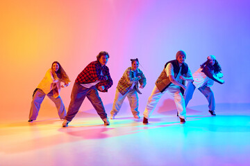 Artistic five dancers, young man and woman in motion, dancing against gradient studio background in neon light. Concept of modern dance style, hobby, active lifestyle, youth culture