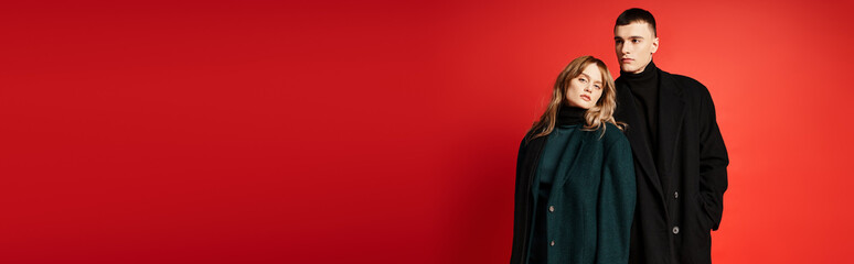 chic pretty woman looking at camera and posing lovingly with her boyfriend on red backdrop, banner