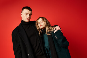 appealing loving couple in sophisticated coats looking at camera on red vibrant background