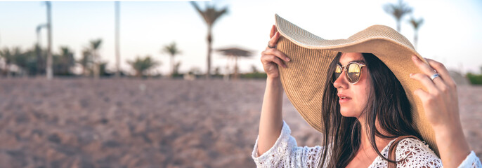 Portrait of a stylish woman with a hat and glasses at sunset on the beach.