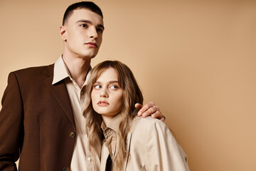 appealing debonair couple in elegant suits posing lovingly and looking at camera on pastel backdrop