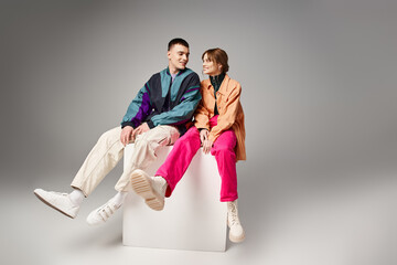 joyous appealing couple in vibrant trendy bombers looking at each other happily on white cube