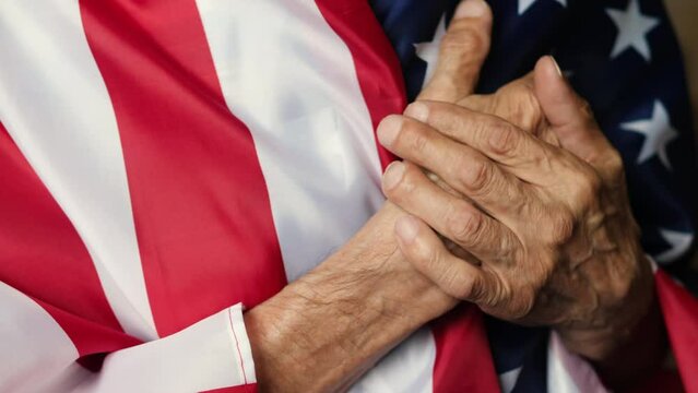 a pensioner holding his heart and the flag of America listens to the national anthem of the country. an elderly man in patriotic feelings sings the anthem