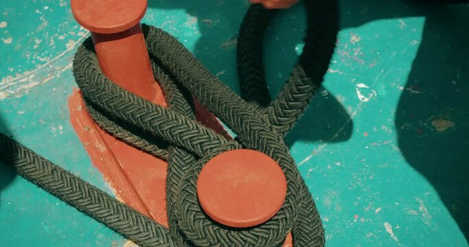 Close-up of a sailor's hand securing a boat with a rope on a cleat. The focused action indicates experience and knowledge of seafaring. A person is working on ship deck.