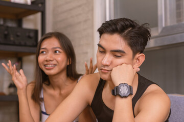 A young asian man looks bored and annoyed, not paying attention to his girlfriends dull and...