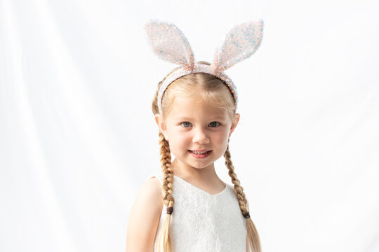 a portrait of a Beautiful blond blue-eyed Caucasian little girl wearing sparkly bunny ears. White background. Easter bunny concept. Two french braids