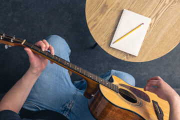 A man with an acoustic guitar and a notepad on the table, top view.