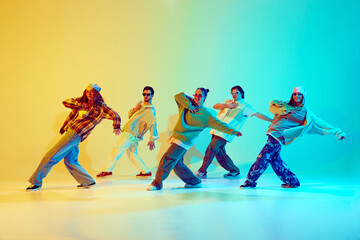 Group of five dancers in casual clothes performing with synchronized poses against gradient green yellow background in neon light. Concept of modern dance style, hobby, active lifestyle, youth culture