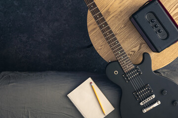 Electric guitar, notepad and music speaker on a table in the room, top view.