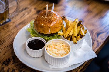 Beef hamburger with lettuce in a sesame bun with barbecue sauce, salad and fries. Food served in a restaurant on a dinner table.