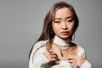 pretty asian young woman in white outfit with heavy makeup and silver necklace on grey background
