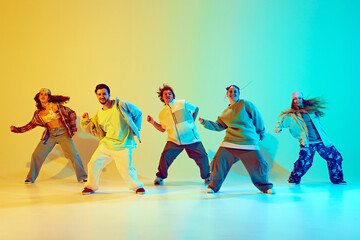Synchronized movements. Group of young people dancing contemp against gradient green yellow background in neon light. Concept of modern dance style, hobby, active lifestyle, youth culture