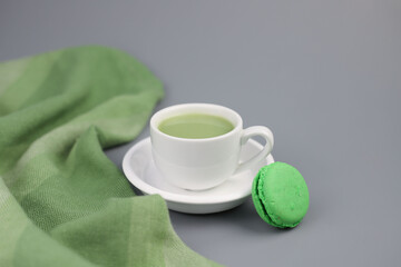 on a gray background, a white cup with matcha green tea and macaroon cookies